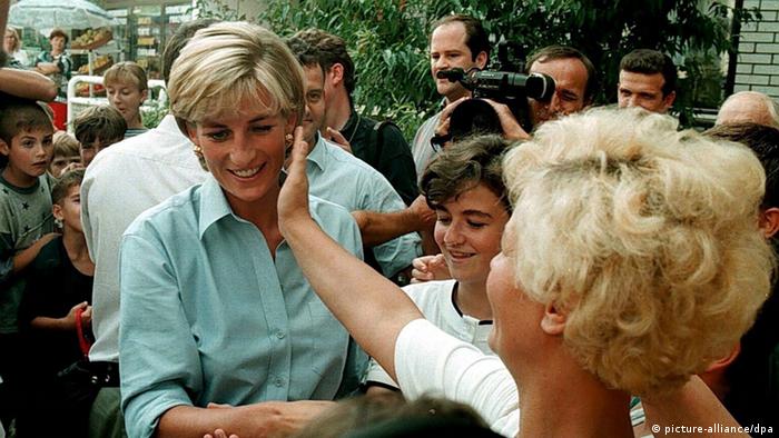 Prinzessin Diana in blauer Bluse unter vielen Menschen, hinter ihr eine Fernsehkamera.