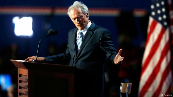 Clint Eastwood stands at a podium with the American flag in the background.