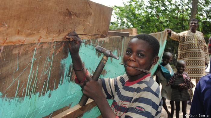 A grinning boy is painting a wooden fishing boat green