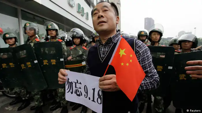 A protester holds a Chinese national flag and a paper bearing slogan as he stands in front of paramilitary policemen on the 81st anniversary of Japan's invasion of China, in Chengdu, Sichuan province, September 18, 2012. Hundreds of Japanese businesses and the country's embassy suspended services in China on Tuesday, expecting further escalation in violent protests over a territorial dispute between Asia's two biggest economies. Chinese characters on the paper read Do not forget 9.18. REUTERS/Jason Lee (CHINA - Tags: POLITICS CIVIL UNREST ANNIVERSARY)