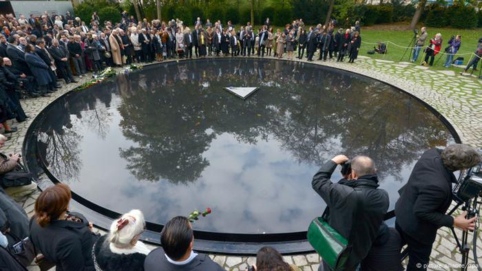 Das Denkmal für die im Nationalsozialismus ermordeten Sinti und Roma in Berlin: eine mit Wasser bedeckte kreisrunde Grantiplatte mit einer kleinen dreieckigen Stele in der Mitte, auf der eine Blume liegt. (Foto: picture alliance/dpa)
