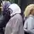 Zwei türkische Frauen mit Kopftüchern gehen an einer jungen blonden Frau vorbei Foto: Roland Weihrauch (dpa)