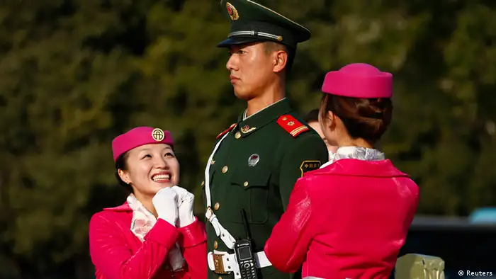 Hotel guides pose for a photo with a paramilitary policeman standing guard on Tiananmen Square near the Great Hall of the People, the venue of the 18th National Congress of the Communist Party of China in Beijing, November 8, 2012. REUTERS/David Gray (CHINA - Tags: POLITICS SOCIETY MILITARY TPX IMAGES OF THE DAY)