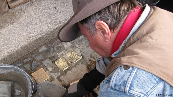 Gunter Demnig bei der Arbeit. Gerade schlägt er mit einer Spitzhacke ein Stück Asphalt aus dem Boden. Foto: Ronny Arnold