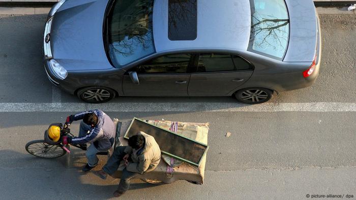 Chinese migrant workers pass a parked car with a bicycle in central Beijing, China, 30 March 2008.