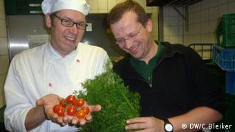 Cassius Garten Küchenchef Arndt Merke und Jan Lüth halten frische Tomaten und Petersilie in der Küche des Restaurants. (Foto: Carla Bleiker/ DW)