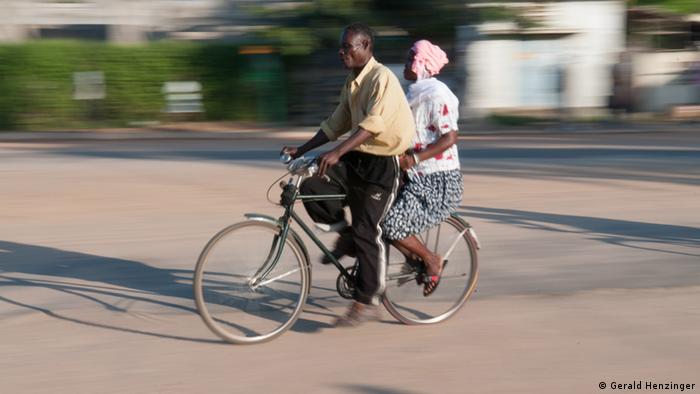 Ein Mann fährt ein Fahrrad, eine Frau sitzt auf dem Gepäckträger.