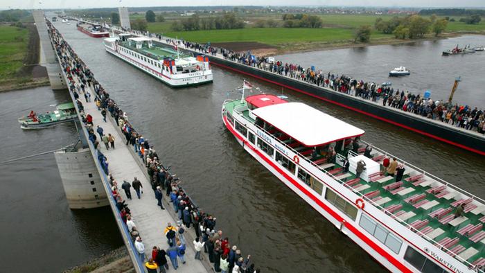 A boat using the Magdeburg Water Bridge while crowds of people watch from the railings. 