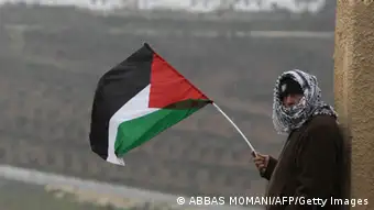 A Palestinian man waves his national flag on the sidelines of a march organized by inhabitants of the West Bank village Nabi Saleh on December 21, 2012, to protest against the expansion of Jewish settlements on Palestinian land. AFP PHOTO/ABBAS MOMANI (Photo credit should read ABBAS MOMANI/AFP/Getty Images)