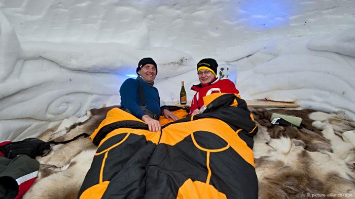 Zwei Menschen in Schlafsäcken in einem Iglu.