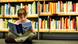 A young girl sits on the floor, reading a book, in front of a large bookshelf A young girl sits on the floor, reading a book, in front of a large bookshelf