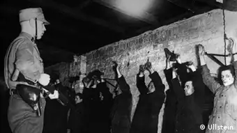 Politische Gegner der Nationalsozialisten nach ihrer Verhaftung im Keller eines SA-Sturmlokals in Berlin, 1933, mit erhobenen und gefesselten Händen an einer Mauer stehend.