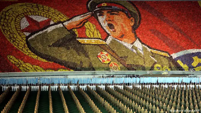 North Koreans perform in front of a display showing a saluting soldier formed by thousands of children holding up cards during the annual massive propaganda spectacle known as a