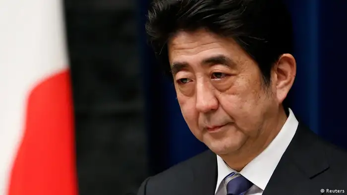 Japan's Prime Minister Shinzo Abe attends a news conference next to the national flag, which is hung with a black ribbon as a symbol of mourning for victims of the March 11, 2011 earthquake and tsunami, at his official residence in Tokyo March 11, 2013. Japan honoured the victims of its worst disaster since World War Two on Monday: the March 11, 2011 earthquake, tsunami and nuclear crisis that killed almost 19,000 people and stranded 315,000 evacuees, including refugees who fled radiation from the devastated Fukushima atomic plant. REUTERS/Yuya Shino (JAPAN - Tags: POLITICS DISASTER ANNIVERSARY)