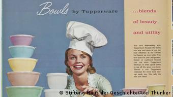 Foto eines Plakates der US-Firma Tupperware. Darauf ist eine lächelnde Frau mit Kochmütze abgebildet, neben ihr liegt ein Stapel bunter Tuppertöpfe. © Stiftung Haus der Geschichte / Axel Thünker