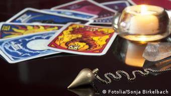 Tarot-Karten, eine Kerze und ein Pendel liegen auf einem Tisch