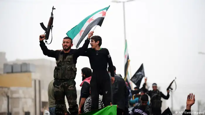 A Syrian youth stands next to a rebel waving a pre-Baath Syrian flag currently used by the opposition during an anti-regime protest in the northern city of Aleppo on March 22, 2013. The UN lamented the escalating violence in Syria and extended a probe into widespread human rights violations in the war-torn country. AFP PHOTO/BULENT KILIC (Photo credit should read BULENT KILIC/AFP/Getty Images)
