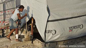 Ein Frau reinigt das Gebiet um ihr Zelt in Haiti (Foto: DPA)