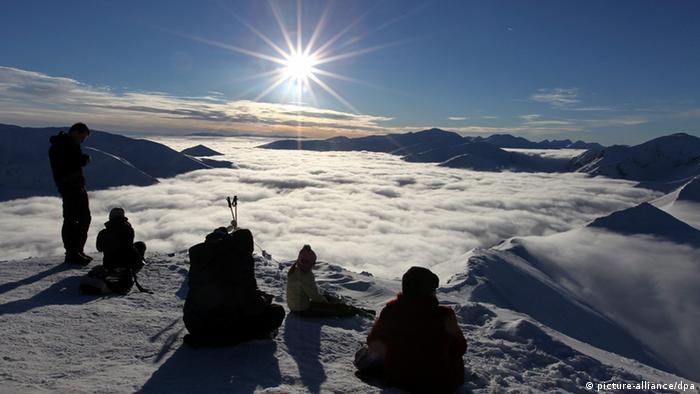 Sylwetki ludzi siedzących na śniegu na tle błękitnego nieba