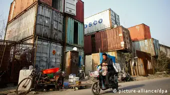 A cycler taking a child drives past homes converted from shipping containers in the suburb of Shanghai, China, 8 March 2013. People stand outside shipping containers serving as their accommodation, as a car passes through a street, in Shanghai. The containers, which house different families, were set up by the landlord, who charges a rent of 500 yuan ($ 80) per month for each container.