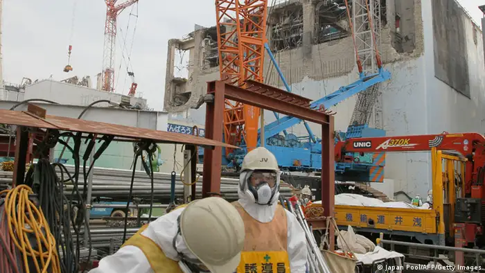 Workers of the Tokyo Electric Power Co (TEPCO) stand in front of the unit four reactor building (R) and unit three reactor building (L) of TEPCO's Fukushima Dai-Ichi nuclear power plant in Okuma Town, in Fukushima prefecture on March 1, 2013, . TEPCO opened up its stricken Fukushima plant to journalists, ahead of the second anniversary of the March 11 disasters. AFP PHOTO / JAPAN POOL via JIJI PRESS JAPAN OUT (Photo credit should read JAPAN POOL/AFP/Getty Images)