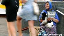 Eine ältere Frau sitzt am 6.8.2003 mit einem Hund im Arm und einem Schild in der Hand an einer Fußgängertreppe in Kiew und lächelnd vorbei eilende junge Passantinen an, in der Hoffnung auf ein Almosen.