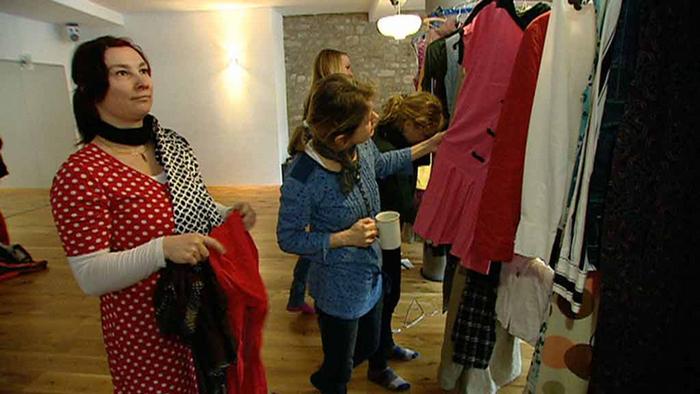 Frauen schauen sich Kleider an, die auf einer Stange hängen.