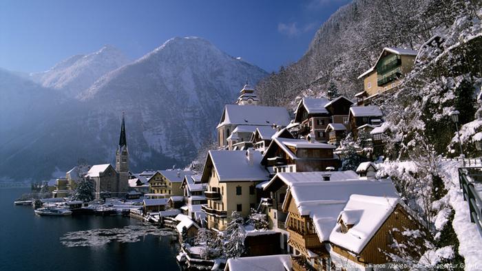 A collection of snow-covered rooftops nestled on the side of a mountain next to a lake