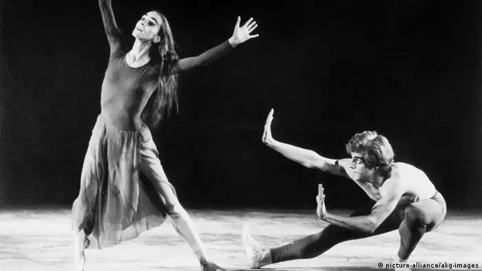 Eine schwarzweiße Fotografie von Pina Bausch, tanzend auf der Bühne und dem Tänzer Iwan Neumann hinter ihr.
(c) picture-alliance/akg-images 