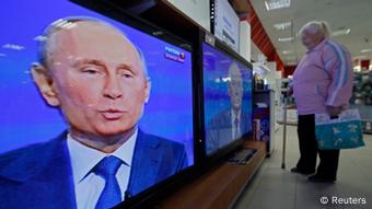 Eine Frau steht vor einem Fernseher, auf dem Wladimir Putin zu sehen ist (Foto: reuters)