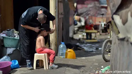 A man cuts the hair of a young boy sat on a chair in a Roma settlement of Belvil in Belgrad, Serbia. Photo: Britta Pedersen/dpa +++(c) dpa - Bildfunk+++