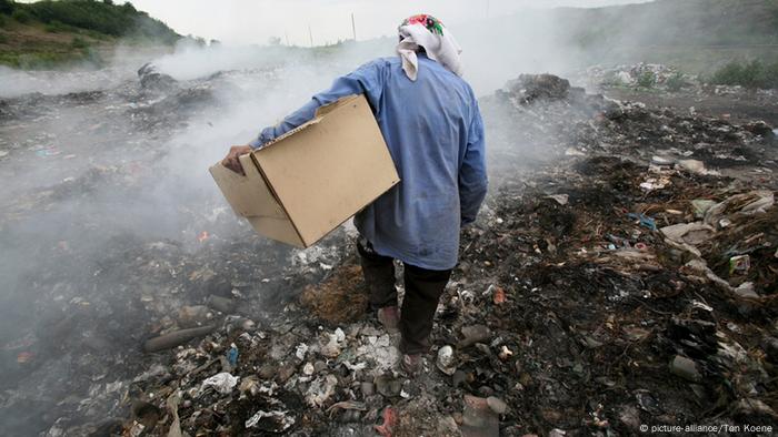 A person carries a cardboard box as they walk through a rubbish dump