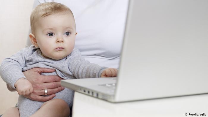 A woman holding a baby at a laptop computer