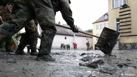 Men wearing battle dress uniforms use a snow shovel to pile up heaps of mud on a German street
(Photo: Michaela Rehle/REUTERS)