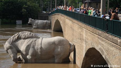 Large statues of a horse and cow disappear under the floodwaters running under a bridge as curious onlookers stare down from above.
(Photo: Frederik Wolf/dpa)