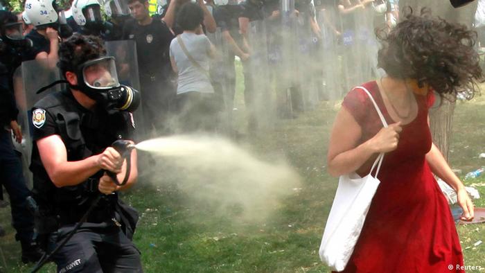 A Turkish riot policeman uses tear gas against a woman as people protest against the destruction of trees in a park brought about by a pedestrian project, in Taksim Square in central Istanbul May 28, 2013.In her red cotton summer dress, necklace and white bag slung over her shoulder she might have been floating across the lawn at a garden party; but before her crouches a masked policeman firing teargas spray that sends her long hair billowing upwards. Endlessly shared on social media and replicated as a cartoon on posters and stickers, the image of the woman in red has become the leitmotif for female protesters during days of violent anti-government demonstrations in Istanbul. Picture taken May 28. REUTERS/Osman Orsal (TURKEY - Tags: CIVIL UNREST)