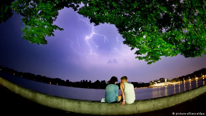 A couple sits on the waterfront and a lightning is seen in the sky
(Foto: picture-alliance/dpa)