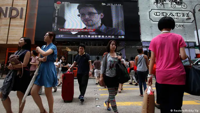 People cross a street in front of a monitor showing file footage of Edward Snowden, a former contractor for the U.S. National Security Agency (NSA), with a news tag (L) saying he has left Hong Kong, outside a shopping mall in Hong Kong June 23, 2013. Snowden left Hong Kong on a flight for Moscow on Sunday and his final destination may be Ecuador or Iceland, the South China Morning Post said. REUTERS/Bobby Yip (CHINA - Tags: POLITICS MEDIA)