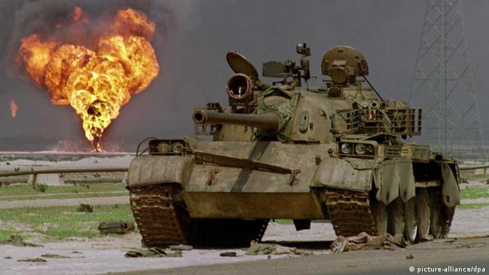 Das Wrack eines verlassenen irakischen Panzers vom Typ T-62 sowjetischer Bauart steht am 02.04.1991 am Rande einer Wüstenstraße in Kuwait während im Hintergrund ein brennendes Bohrloch des Al-Ahmadi Ölfeldes zu sehen ist. (Foto: dpa - Bildfunk)