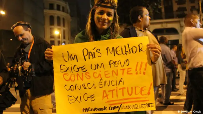 Eine junge Frau, die in eine brasilianische Flagge gehüllt ist, hält ein Plakat hoch