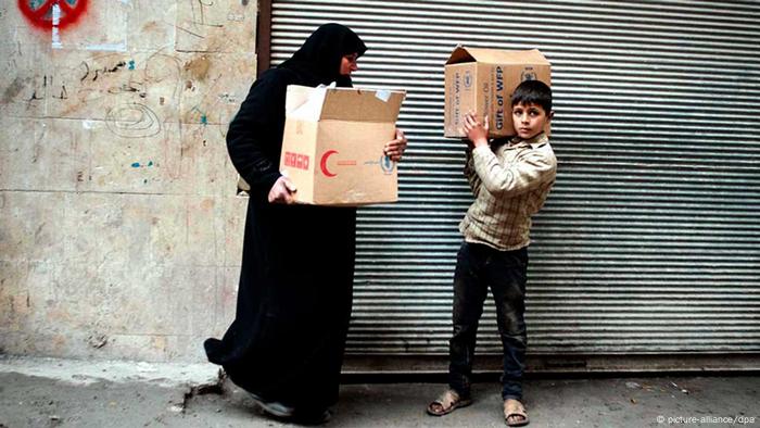 Mulher síria e filho carregam caixa com alimentos em Aleppo, em 2013