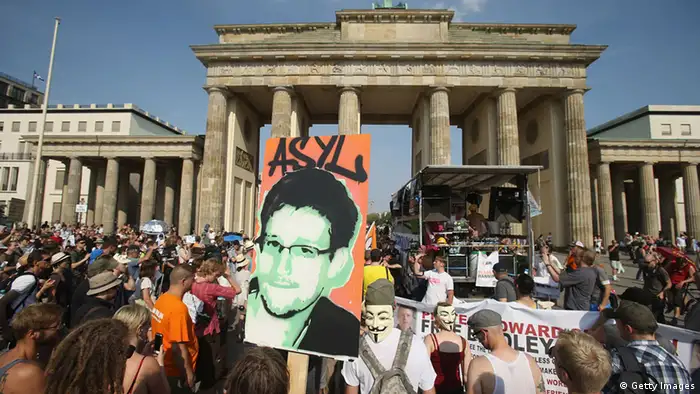 BERLIN, GERMANY - JULY 27: A participant holds up a picture of former NSA employee Edward Snowden with the word 'asylum' written above it at a protest gathering in front of the Brandenburg Gate against the electonic surveillance tactics of the NSA on July 27, 2013 in Berlin, Germany. The NSA scandal has been especially contentious in Germany after media reports claimed the NSA had conducted wide scale gathering of electonic data, including e-mails, of German citizens. Activists are demonstrating against the NSA in cities across Germany today. (Photo by Sean Gallup/Getty Images)