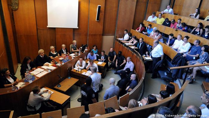 Zdjęcie przedstawia salę sądową podczas procesu, sędziowie siedzą za stołem po lewej stronie, ławy publiczności są pewne