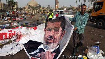 Ein Mann hebt ein zerknittertes Mursi Poster von der Starße auf. (Foto: AP Photo/Amr Nabil)