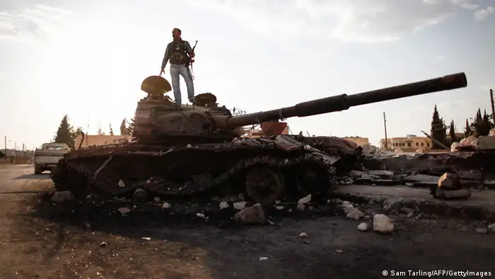 An armed fighter of the Free Syrian Army stands atop a destroyed Syrian army tank to have his picture taken by a passer-by in the northern Syrian town of Azaz, some 47km north of Aleppo, on September 10, 2012, as UN envoy Lakhdar Brahimi admitted he faced a 'very difficult' task in his bid to end the nearly 18-month conflict. AFP PHOTO/SAM TARLING (Photo credit should read SAM TARLING/AFP/GettyImages)