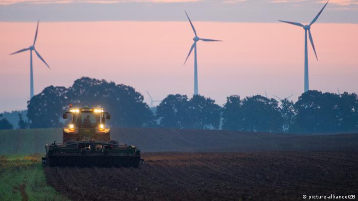 Трактор вспахивает поле на рассвете, на заднем плане ветряки