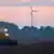 Трактор вспахивает поле на рассвете, на заднем плане ветряки