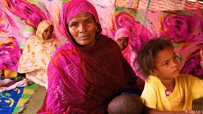 Wrapped in a vibrant pink scarf, Schweda, sits on the ground with one of her children