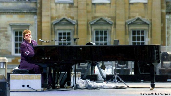 Elton John on the piano, wearing a purple suit.