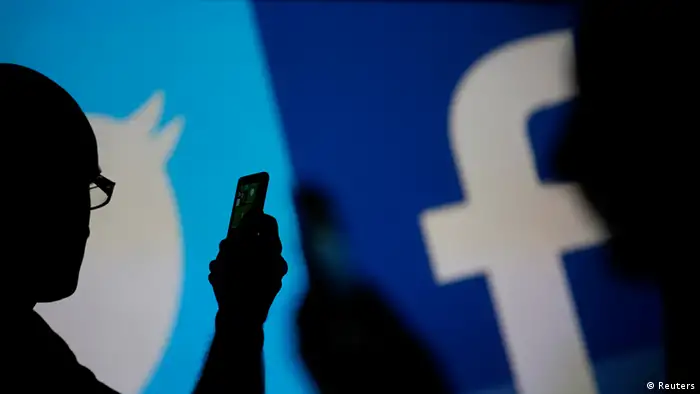 Men are silhouetted against a video screen with Facebook and Twitter logos as they pose with a Nokia Lumia 820 and Samsung Galaxy S4 in this photo illustration taken in the central Bosnian town of Zenica, August 14, 2013. REUTERS/Dado Ruvic (BOSNIA AND HERZEGOVINA - Tags: BUSINESS TELECOMS)